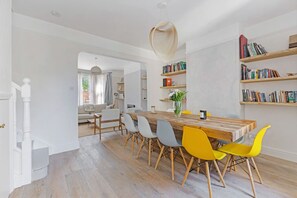 Een ruime eethoek met een houten tafel en stoelen, een hanglamp en boekenkasten vol boeken.