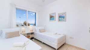 Un dormitorio con dos camas, una ventana con vista al mar y un mueble bajo con cajones.