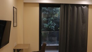 Una habitación de hotel con una cama, una silla, un televisor montado en la pared y un amplio ventanal con cortinas.