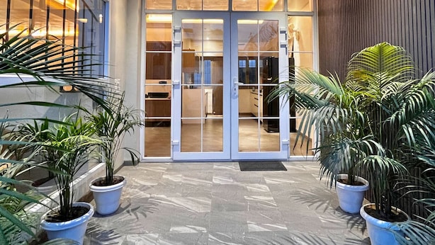 Una entrada moderna a un edificio con puertas de vidrio, plantas en macetas y un ventilador de techo.