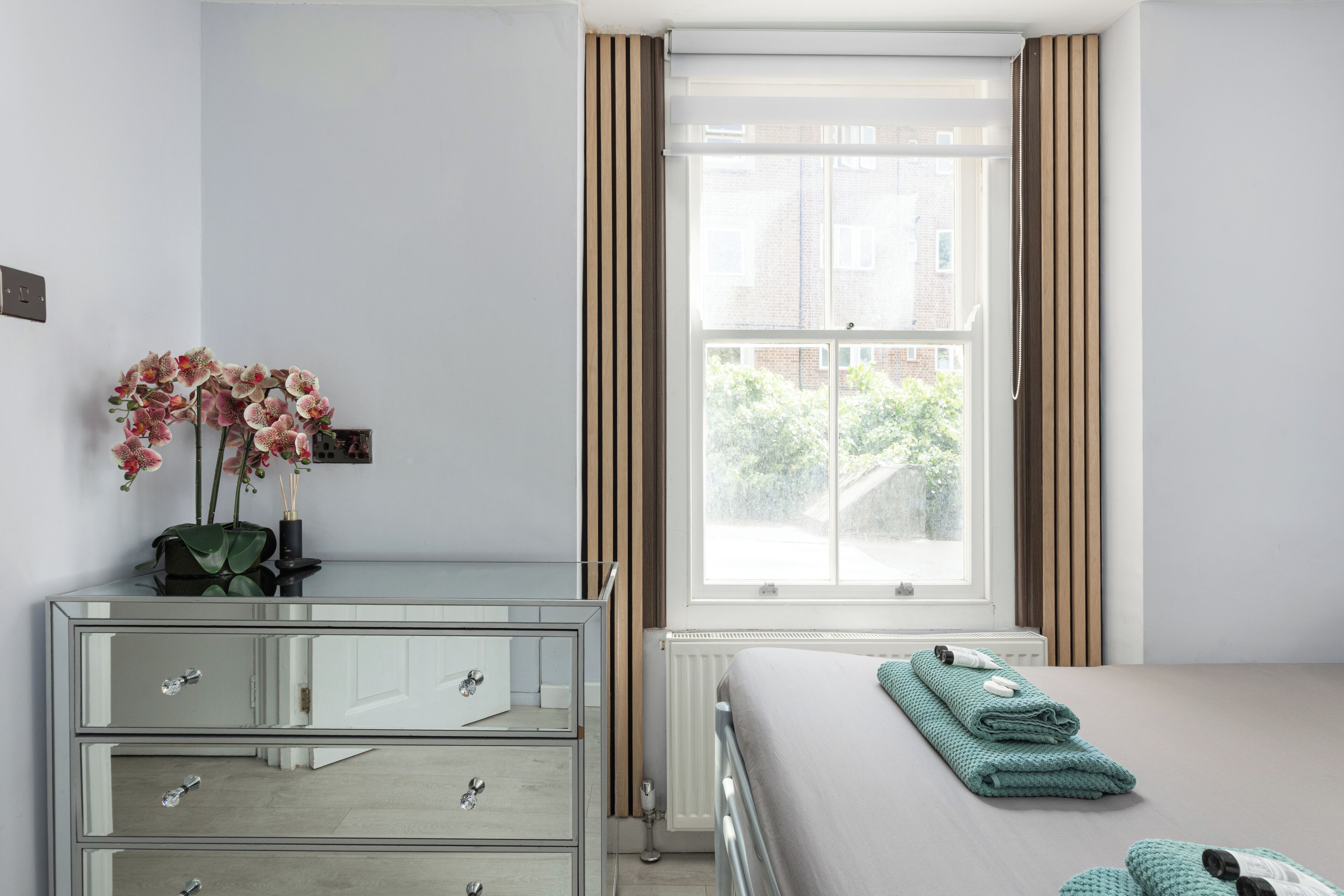 A bedroom with a bed, a dresser, a window with curtains, and a view of the outside.