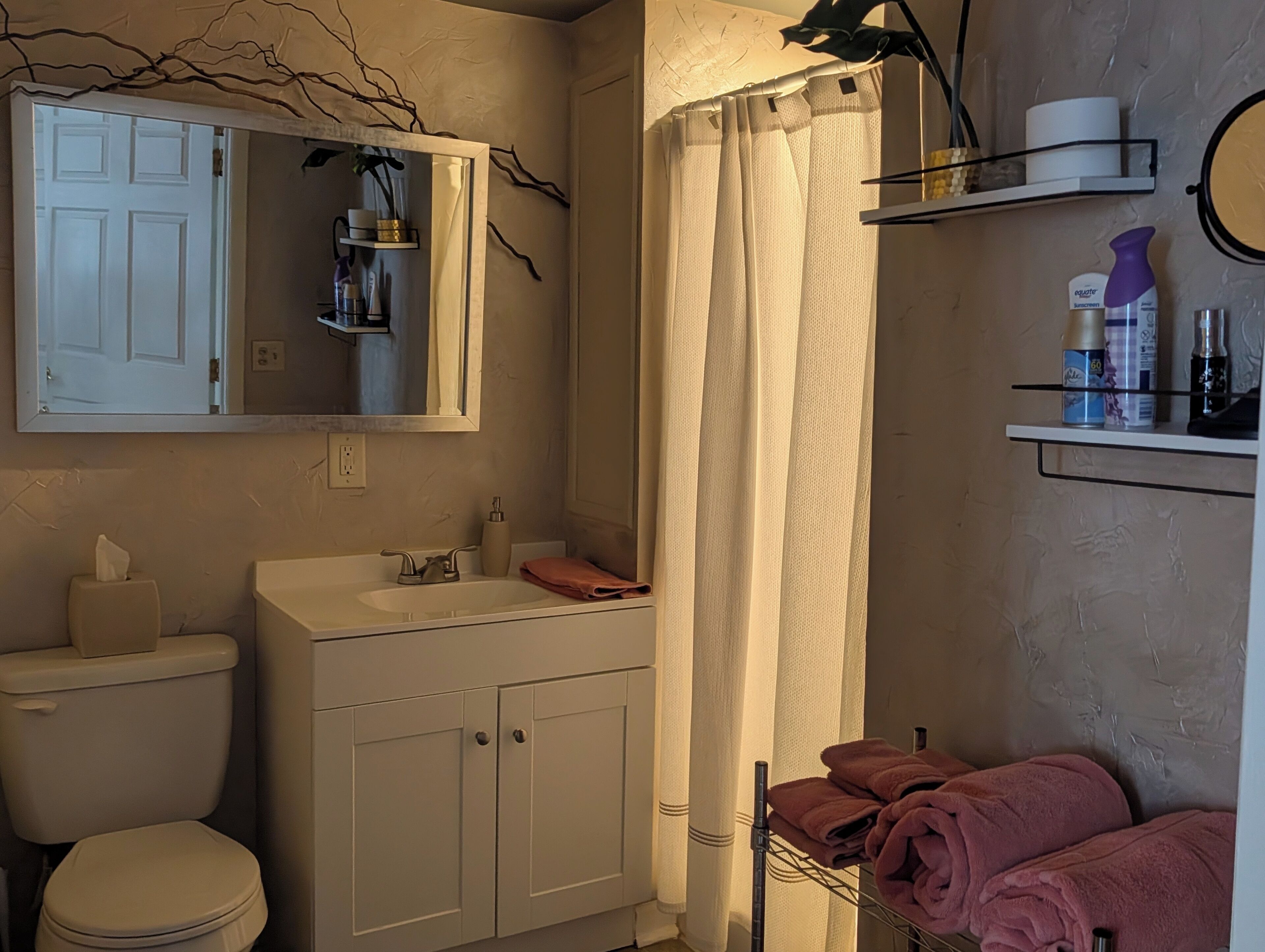A bathroom with a toilet, sink, mirror, shower curtain, and a towel rack with towels.