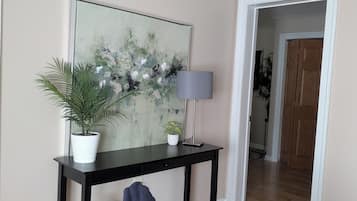 Une pièce avec une console noire, une plante en pot, une lampe et un tableau accroché au mur.