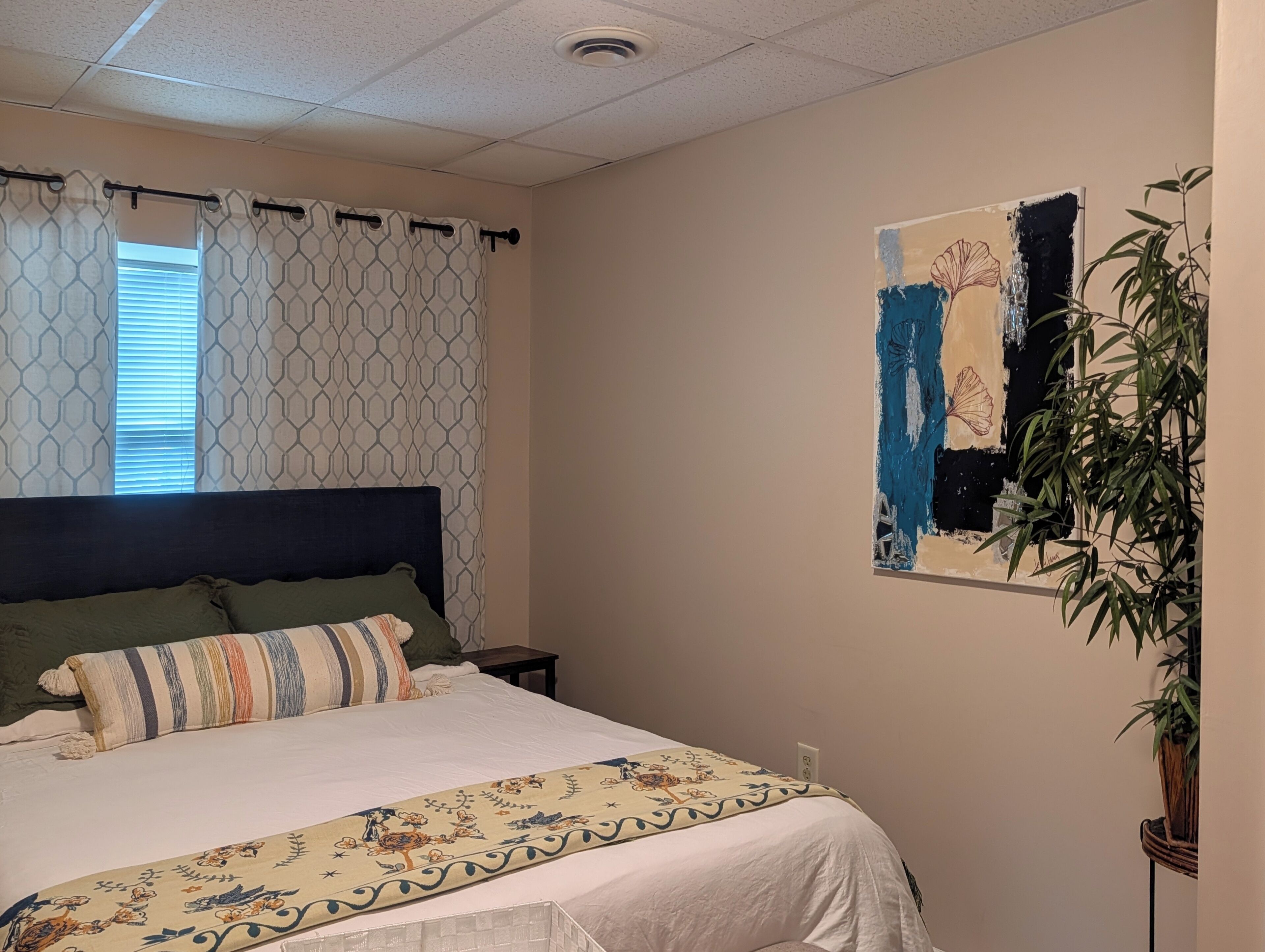 Une chambre à coucher avec un lit, une table de chevet, un tableau accroché au mur et une plante en pot.