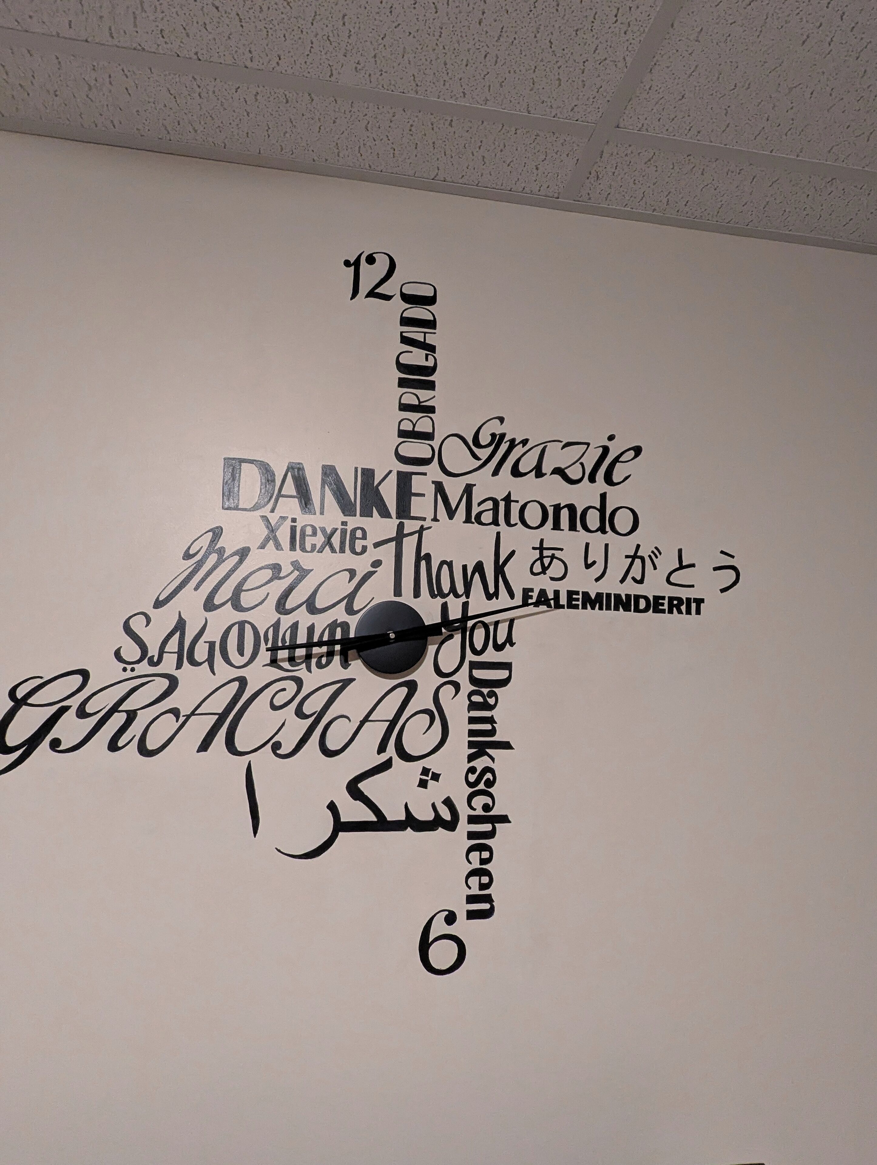 Un mur orné d’une horloge et de divers mots, écrits dans différentes langues, exprimant la gratitude.