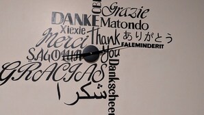 Un mur orné d’une horloge et de divers mots, écrits dans différentes langues, exprimant la gratitude.