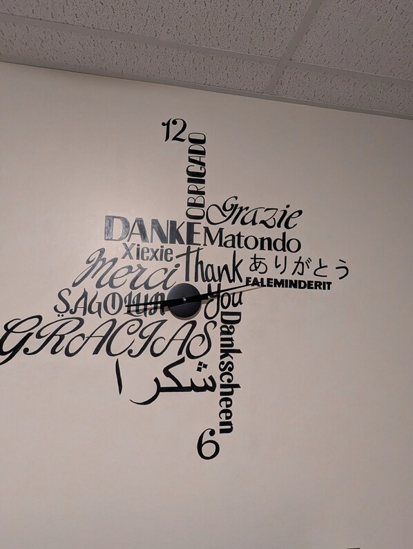 A wall with a clock and various words in different languages expressing gratitude.