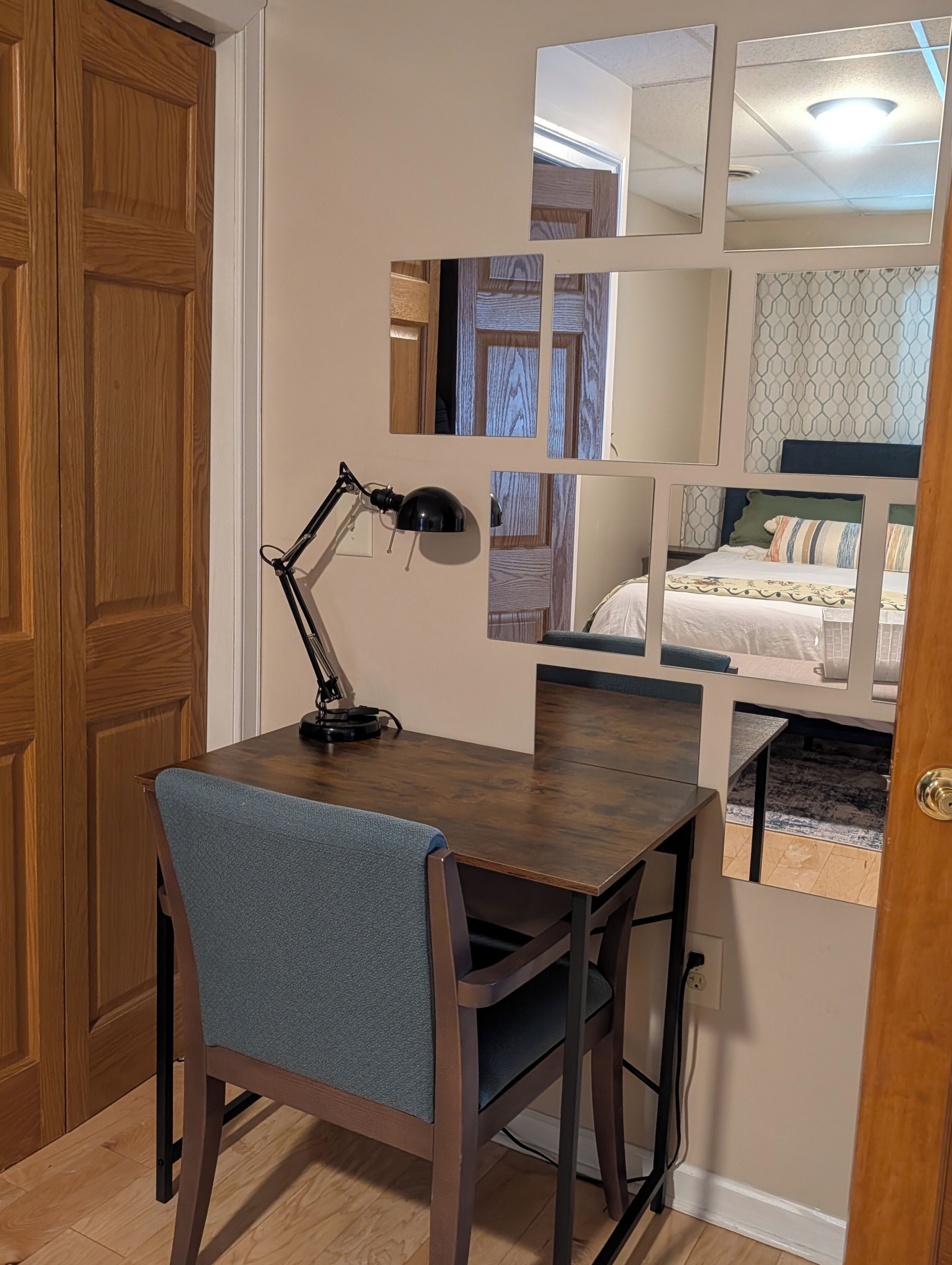 Una habitación con un escritorio de madera, una silla, una lámpara de escritorio y una cama con cabecera estampada.