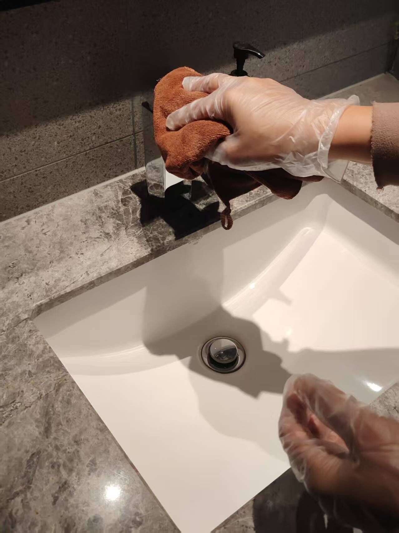 Una mano sosteniendo un paño marrón cerca de un lavabo con desagüe.