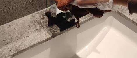 Una mano sosteniendo un paño marrón cerca de un lavabo con desagüe.
