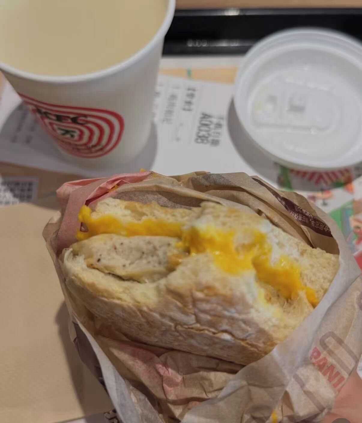A breakfast sandwich with egg and cheese, a cup of coffee, and a container of yogurt.