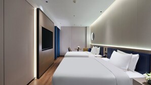 Ein modernes Hotelzimmer mit einem großen Bett, einem Flachbildfernseher, einem Nachttisch und einem kleinen runden Tisch mit einer Lampe.