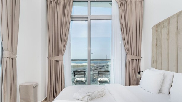Ein Hotelzimmer mit einem großen Bett, beigen Vorhängen und Blick auf eine Brücke und einen Strand.