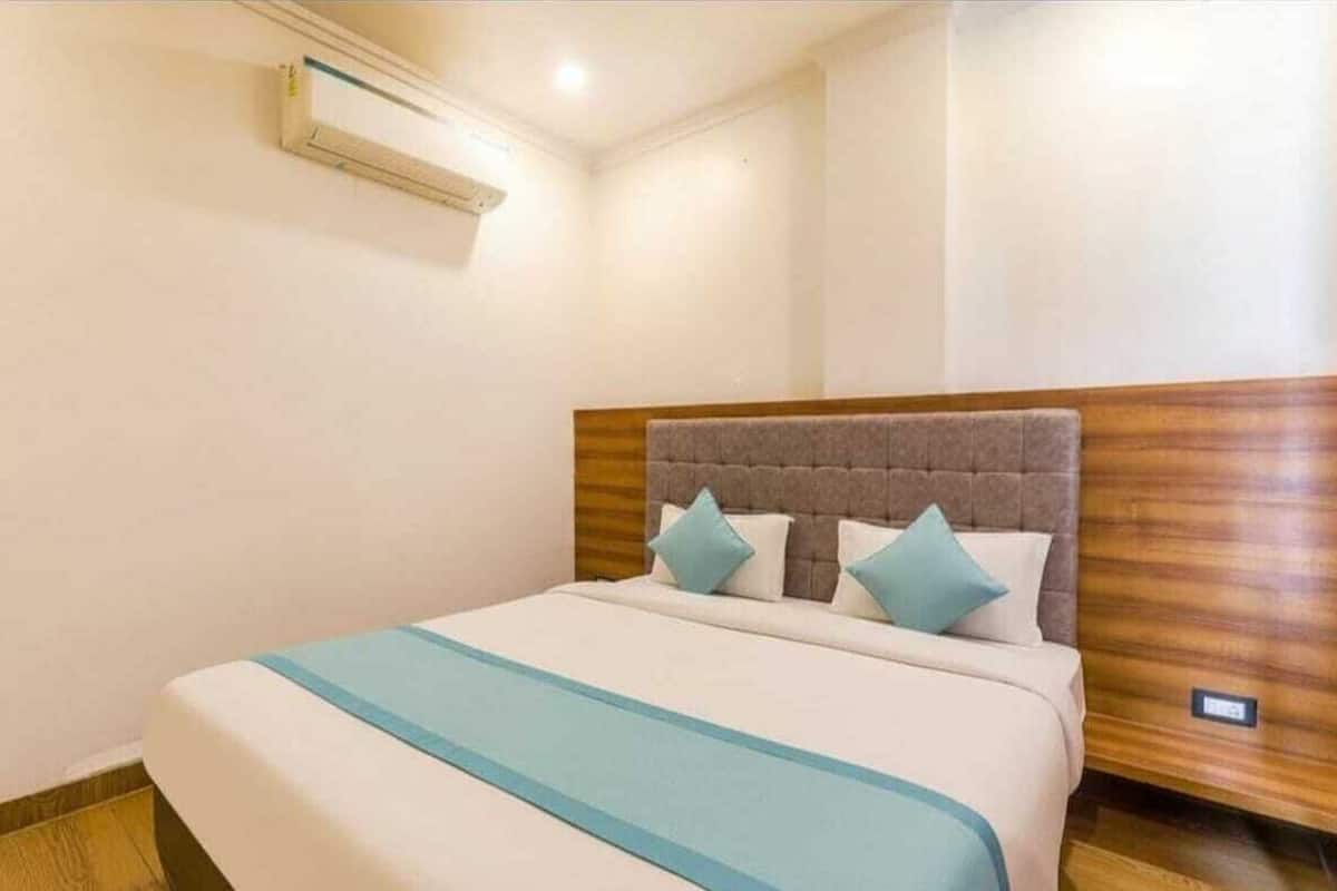 Una habitación de hotel con una cama, cabecera de madera y aire acondicionado instalado en la pared.