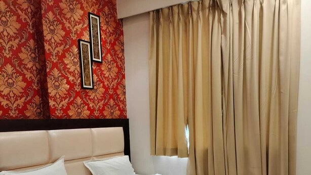 A hotel room with a large bed, a headboard, a red patterned wall, and beige curtains. - Hotel Golden Crown - 600m to Kashi Vishwanath Temple (Varanasi)