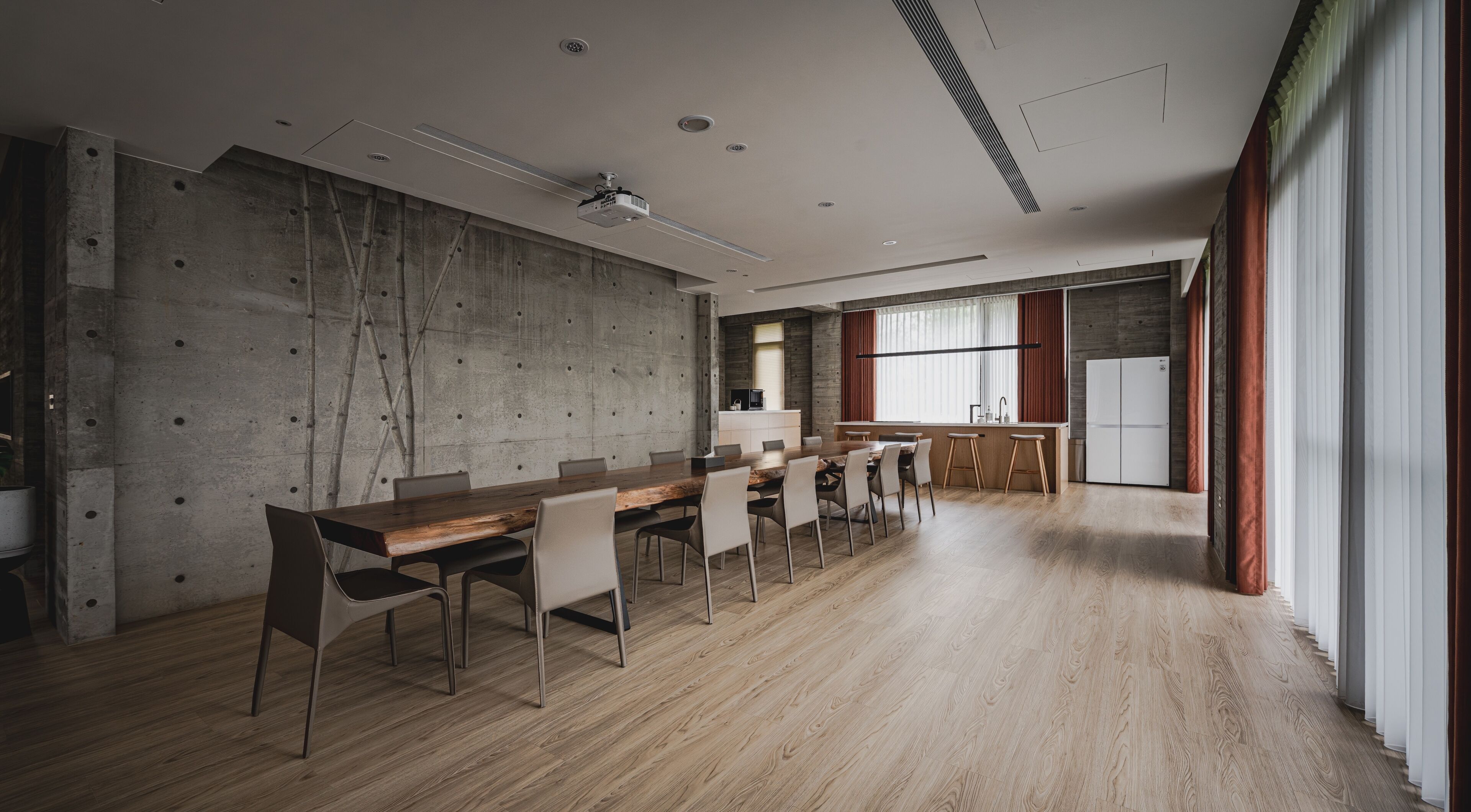 A modern conference room with a long table, chairs, a projector, and a kitchen area.