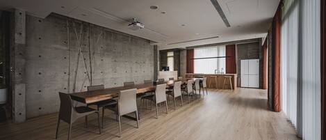 A modern conference room with a long table, chairs, a projector, and a kitchen area.