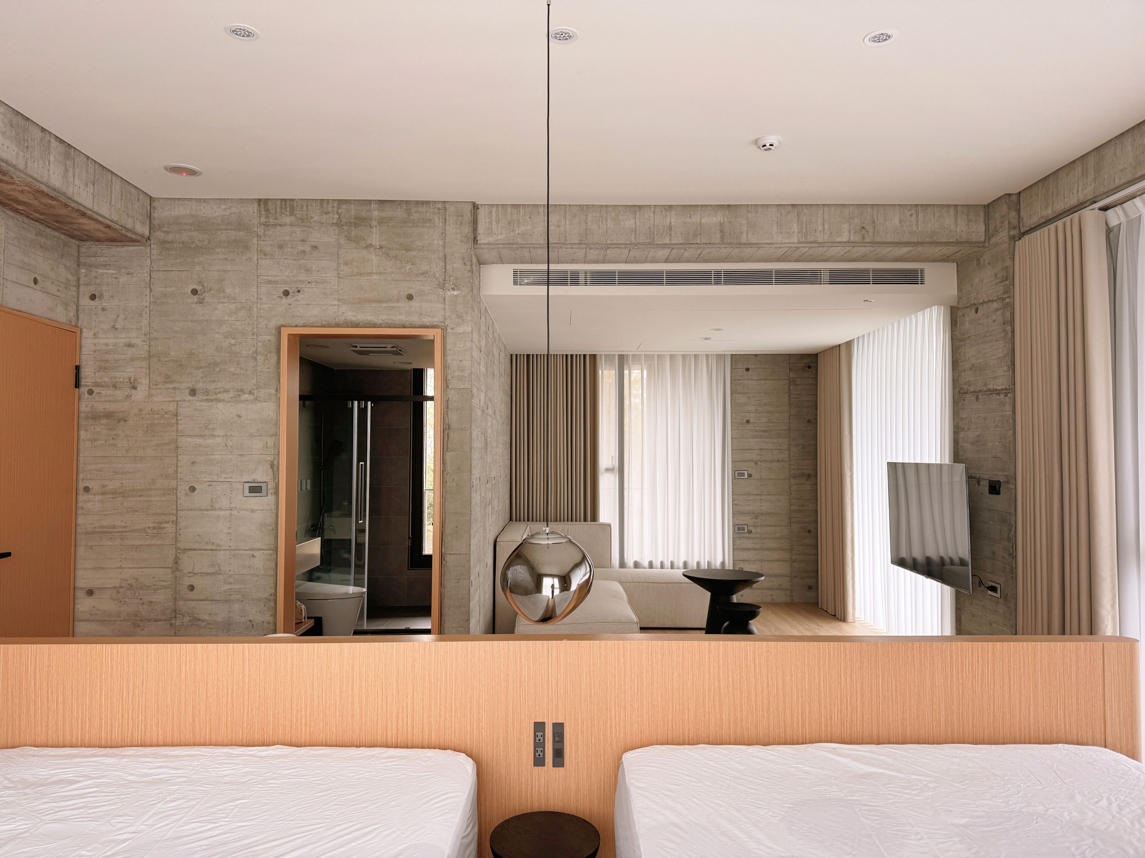 A modern hotel room with a large bed, a seating area, a TV, and a bathroom visible through an open door.