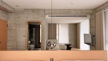 A modern hotel room with a large bed, a seating area, a TV, and a bathroom visible through an open door.