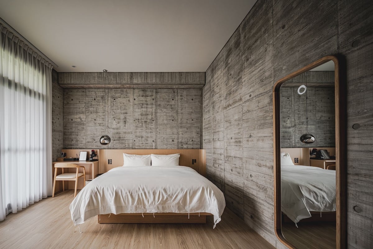 A modern bedroom with a wooden headboard, a large mirror, a wooden desk, and a bed with white bedding.