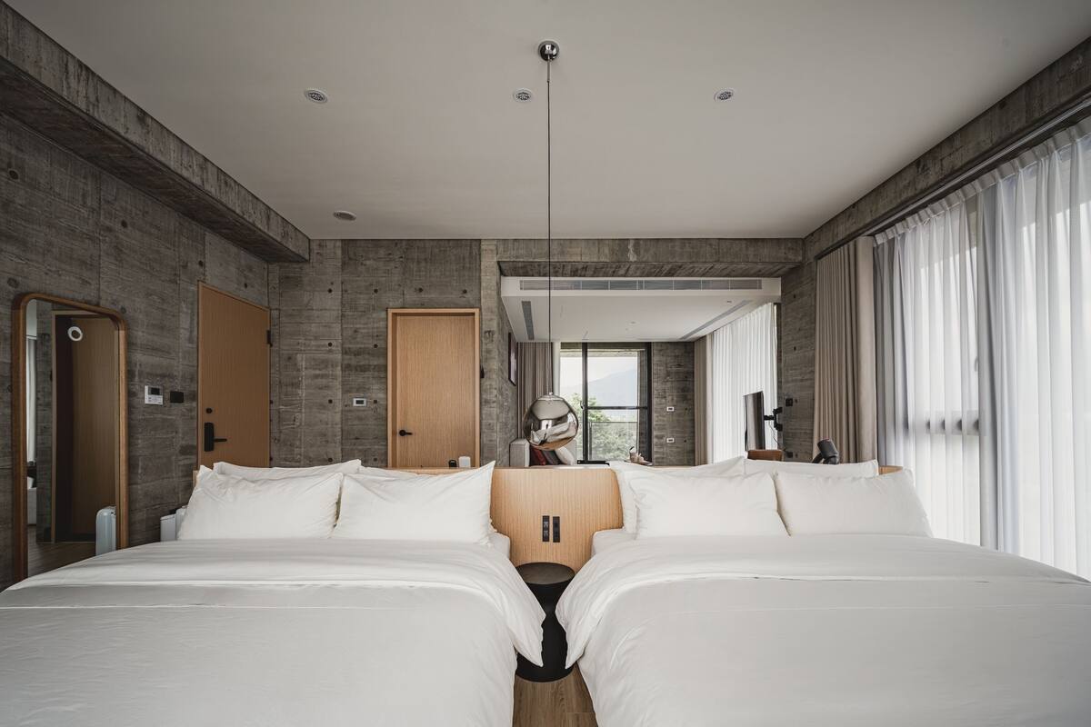 A modern hotel room with a large bed, a wooden wardrobe, and a large window with curtains.