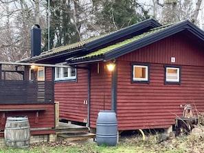 Una cabaña de madera roja con techo negro, una chimenea y un pequeño porche con escalones que llevan a la puerta.