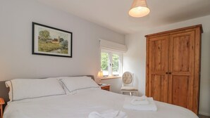 A neatly made bed with white linens and two folded towels, a wooden wardrobe, a framed landscape painting, and a window with a view of greenery. - Greenham Rise (Stoke-sub-Hamdon)