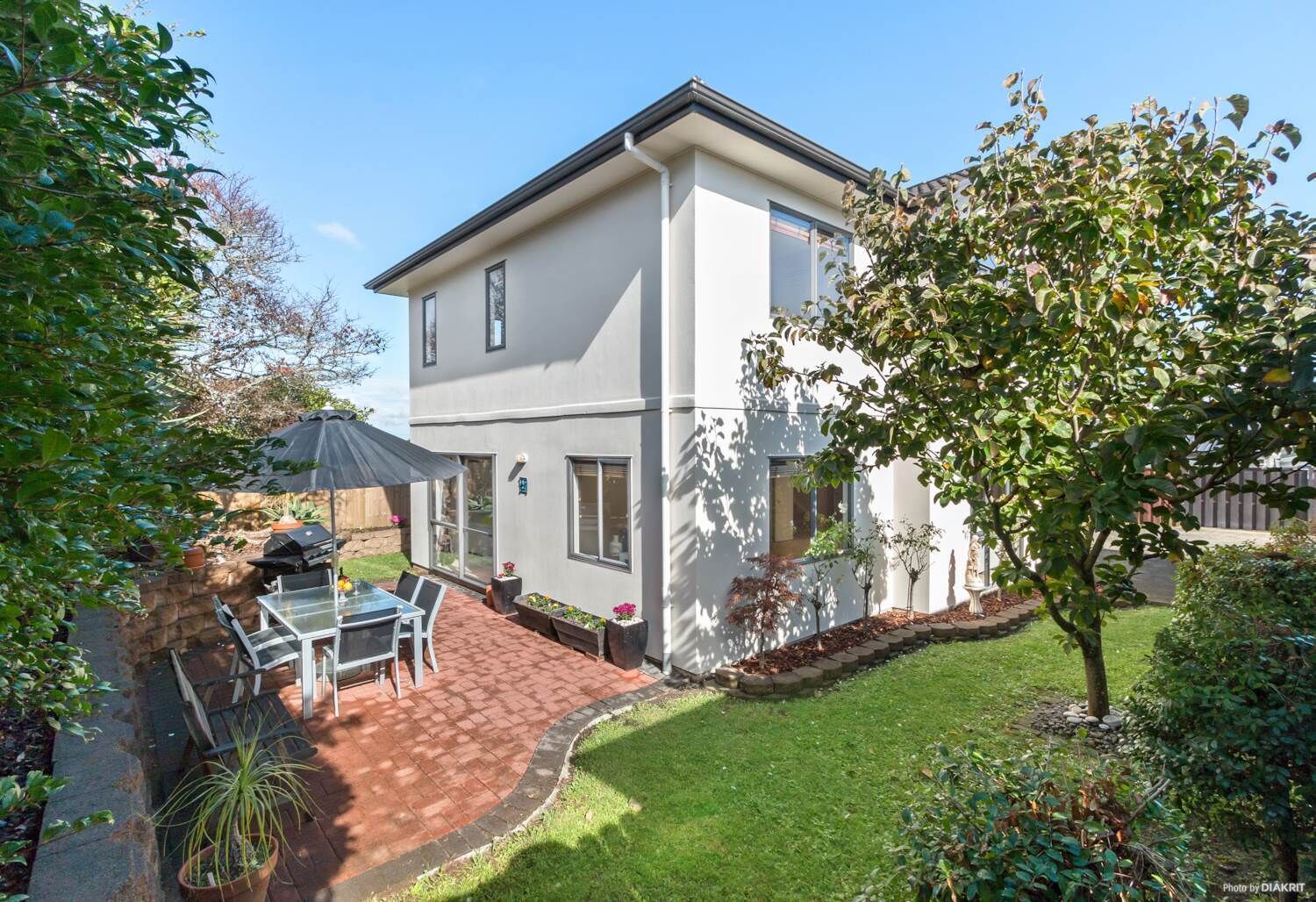 Une maison à deux étages dotée d’un patio, d’un barbecue et d’un petit jardin.