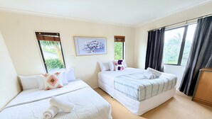 Ett hotellrum med två sängar, ett stort fönster med gardiner, en tavla på väggen och ett träskåp.