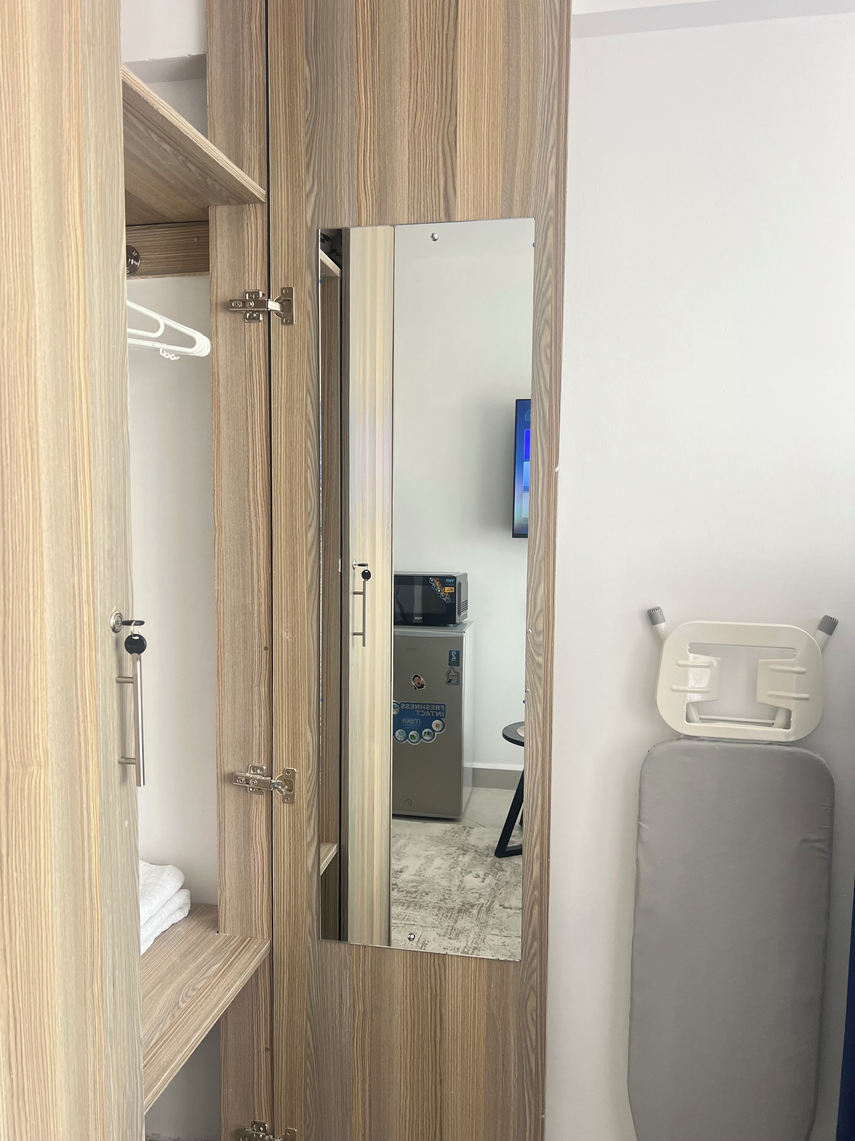 A wooden wardrobe with a mirror, a microwave, and a small table with a chair.