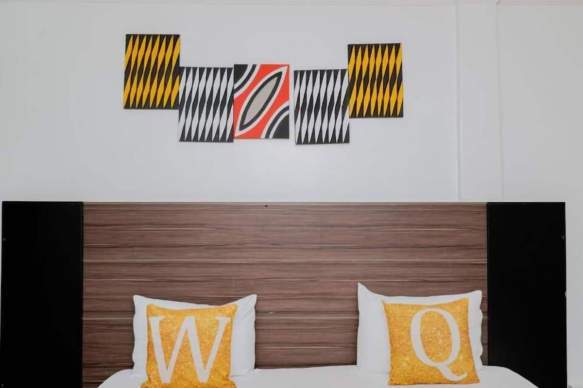 Ein Hotelzimmer mit einem hölzernen Kopfteil, zwei Kissen mit großen Lettern und einem Wandbild über dem Bett.