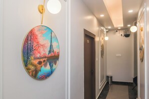 Een gang met een aan de muur hangend schilderij van de Eiffeltoren, een deur met de aanduiding '201' en een afvalbak.