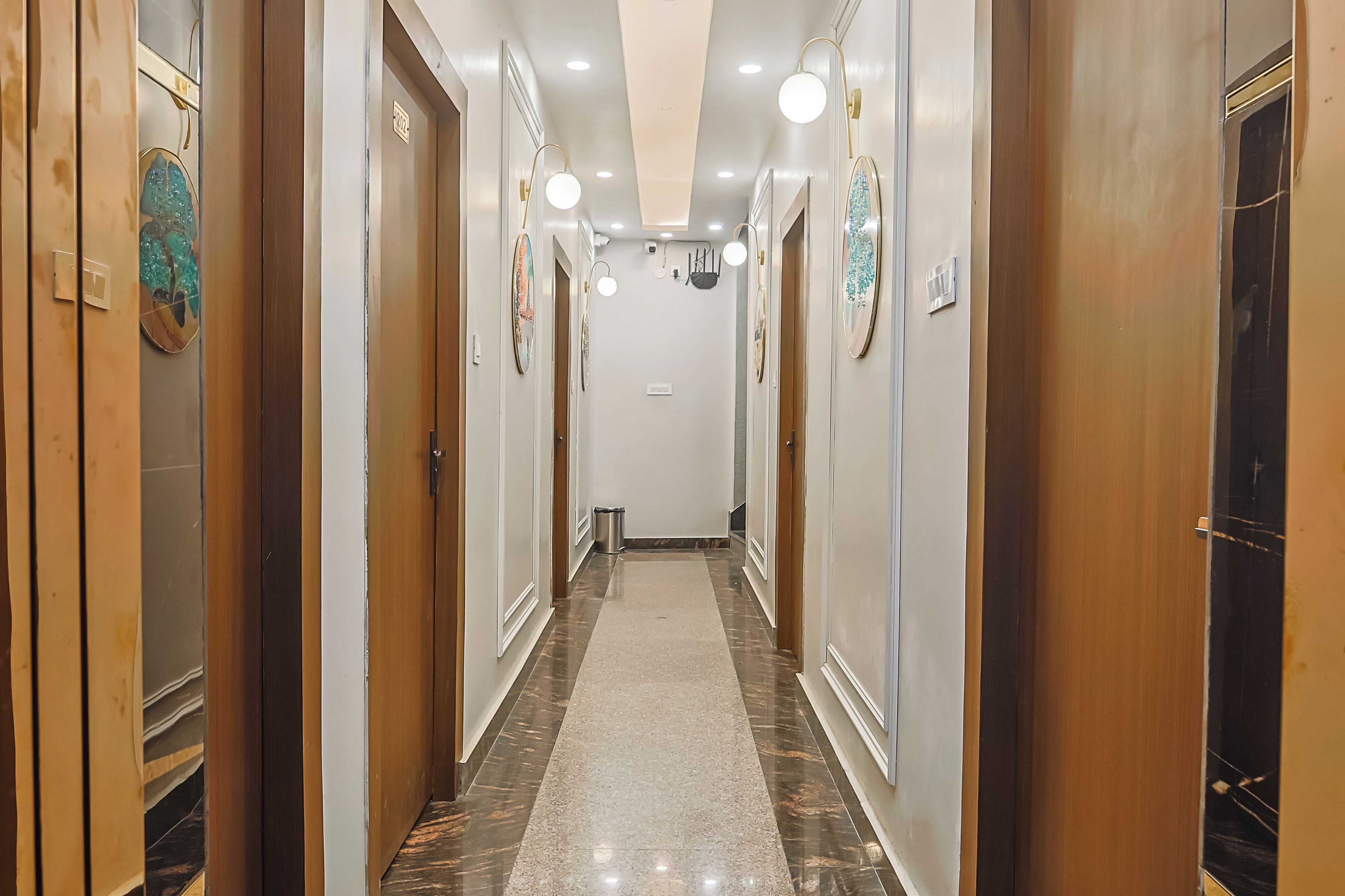 A hotel corridor with wooden doors, a marble floor, and wall-mounted light fixtures.
