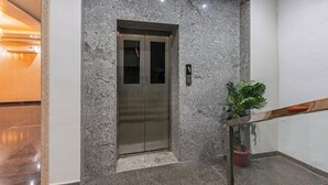 A modern elevator with a metallic finish, a granite wall, and a potted plant beside a staircase. - Treebo Sloka Residency (Ranchi)
