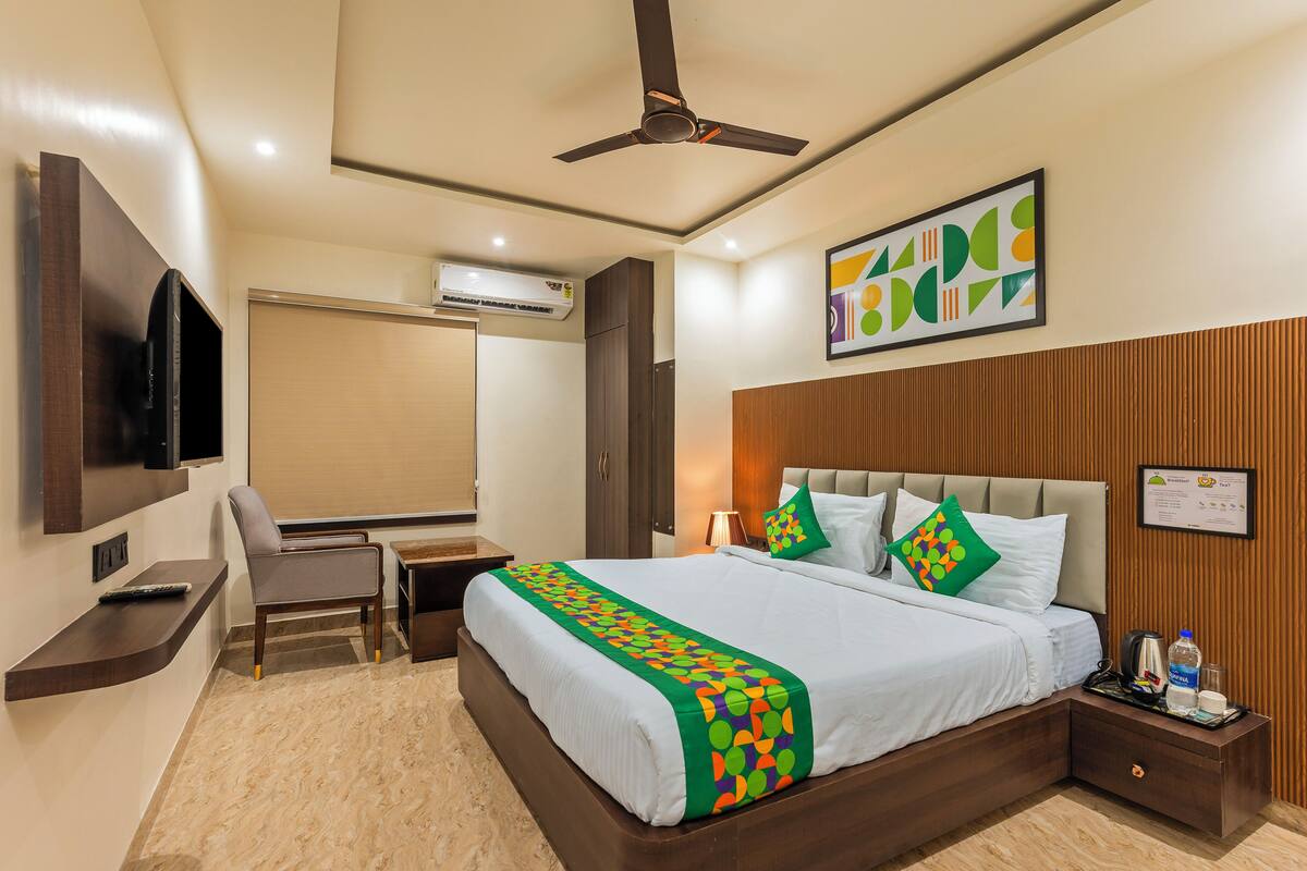 A hotel room with a bed, a desk, a chair, a TV, a ceiling fan, and a wall-mounted artwork.