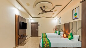 A hotel room with a flat-screen TV, two beds with colorful bedspreads, a ceiling fan, and a door. - Treebo Sloka Residency (Ranchi)