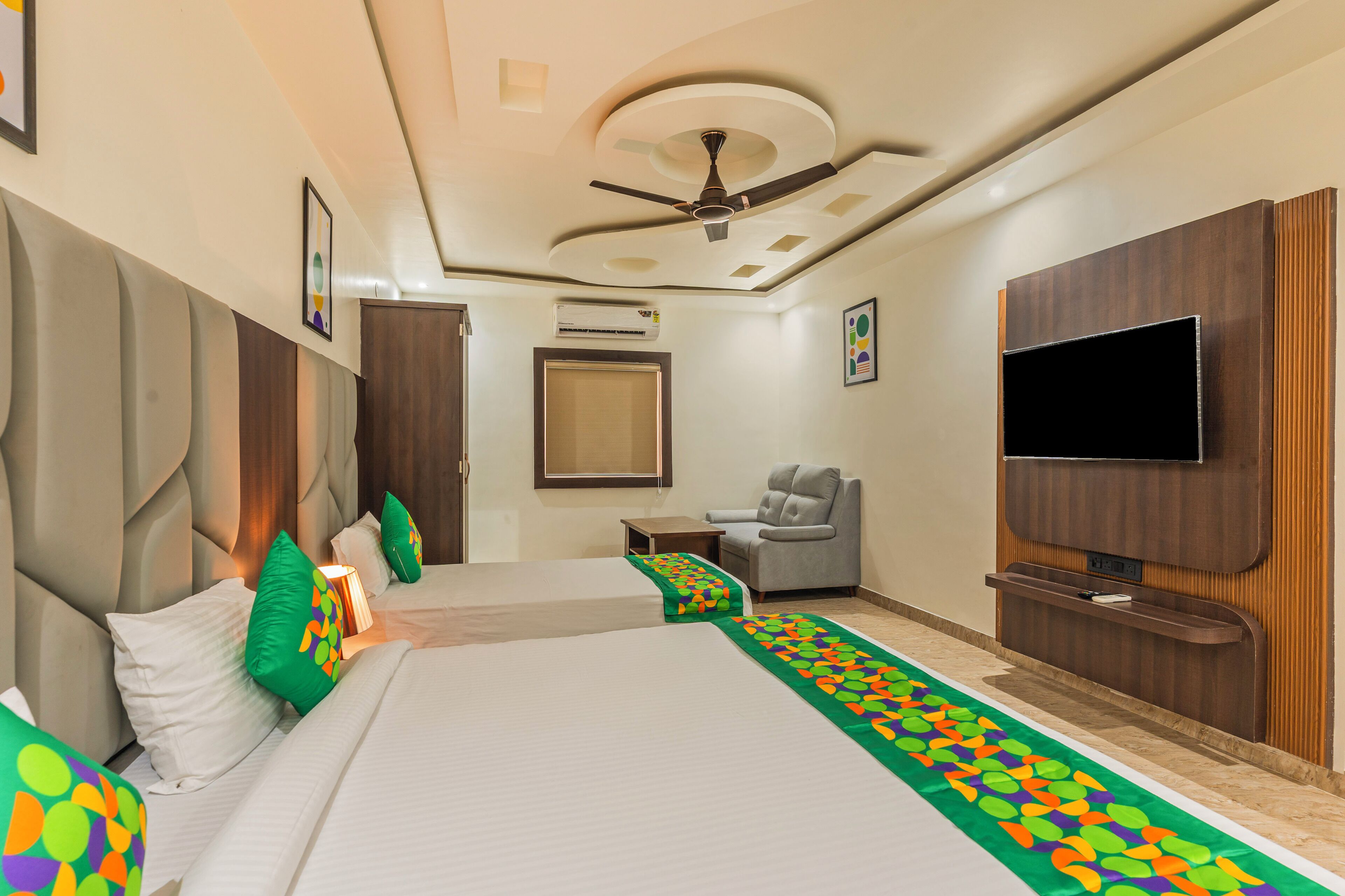 Habitación de hotel con una cama grande, televisor, ventilador de techo y una pequeña zona de estar.