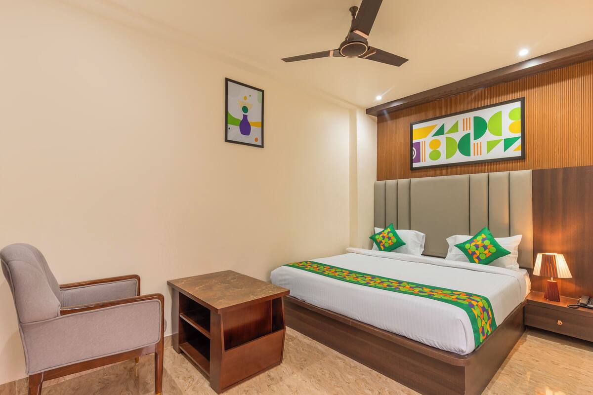 A hotel room with a bed, a chair, a nightstand, a ceiling fan, and artwork on the walls.