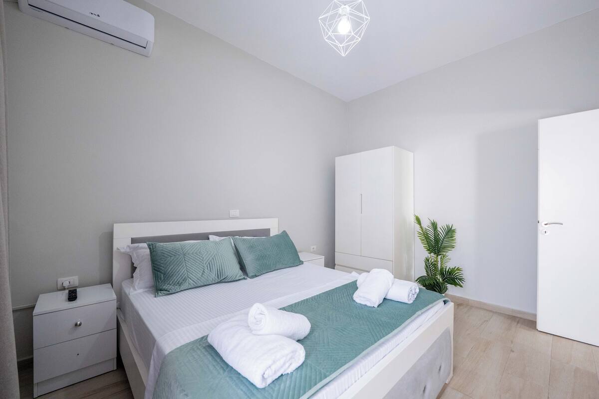 A modern bedroom with a bed, nightstand, wardrobe, and a ceiling light fixture.