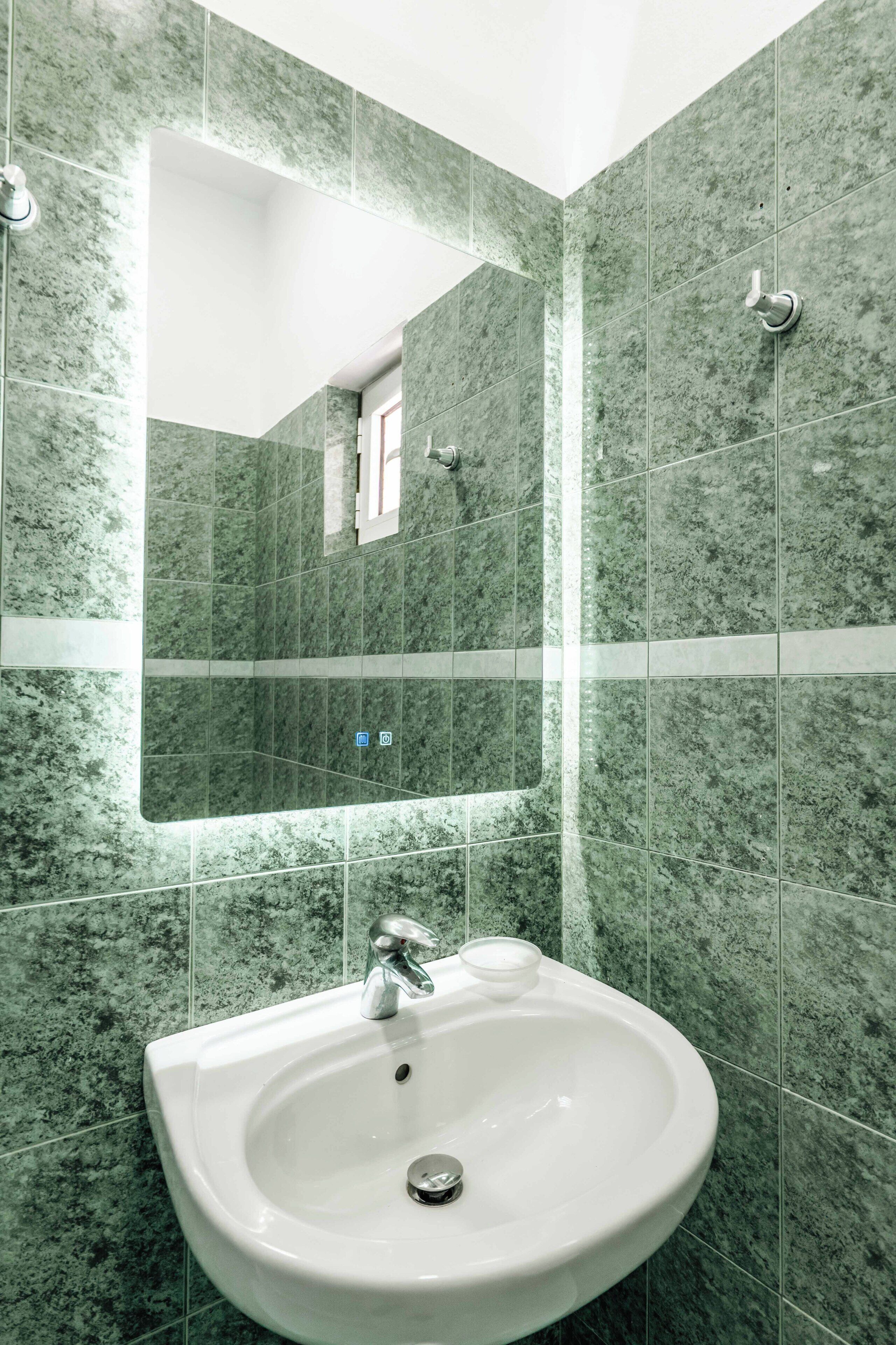 A bathroom with a white sink, green marble tiles, a mirror, and a window.