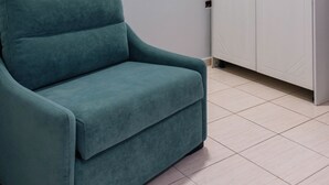 Ein blaugrünes Sofa, ein weißer Kleiderschrank und ein Fliesenboden in einem Zimmer.
