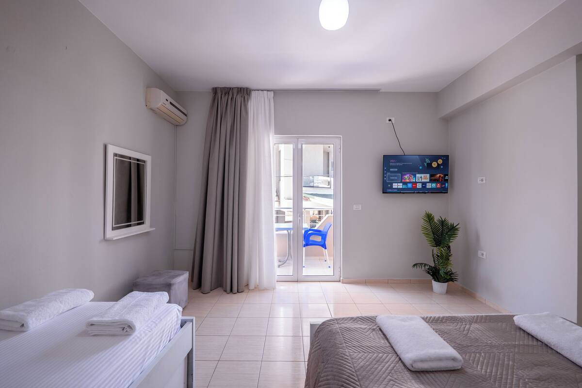 A modern hotel room with a bed, a TV, a plant, and a view of the outside.