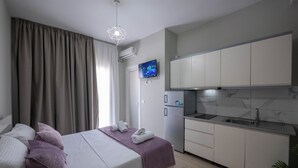 Ein Schlafzimmer mit Bett, Kissen, einem Fernseher, einer Küche mit Schränken, einem Kühlschrank und einer Pflanze.