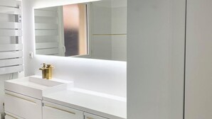Et moderne badeværelse med et hvidt toiletbord, et stort spejl og en guldfarvet vandhane.
