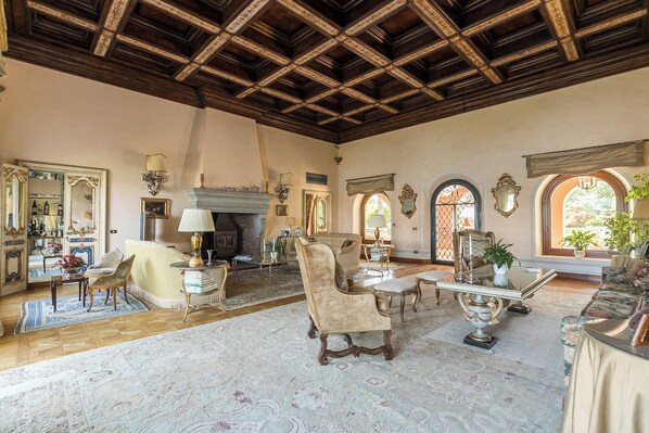 A spacious living room with a high wooden ceiling, a fireplace, and a large arched window.