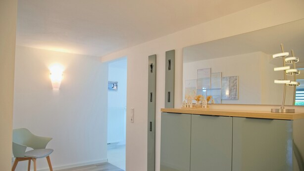 A modern interior with a light-colored floor, a green chair, a wooden counter, and a large mirror. - Spacious, allergy-friendly accommodation in the basement near the beach and town (Grömitz)