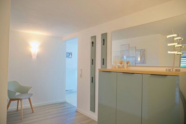 Ein modernes Interieur mit hellem Boden, einem grünen Sessel, einer Holzauslage und einem großen Spiegel.