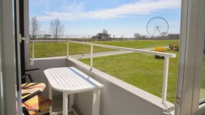 A balcony with a table and chairs, a view of a grassy area, and a Ferris wheel in the distance. - Comfortable Apartment Hanseat II App. 121 with sea view and balcony in Grömitz (Grömitz)