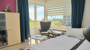 A hotel room with a bed, a chair, a small table, a cabinet, and a window with a view of a Ferris wheel. - Comfortable Apartment Hanseat II App. 121 with sea view and balcony in Grömitz (Grömitz)
