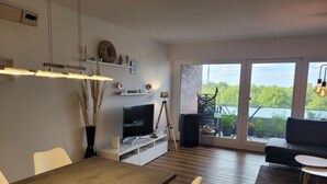 A modern living room with a dining area, a flat-screen TV, and a balcony with potted plants. - Comfortable vacation apartment Seeadler 30 with balcony near Friesenstrand in Tossens (Butjadingen-Tossens)